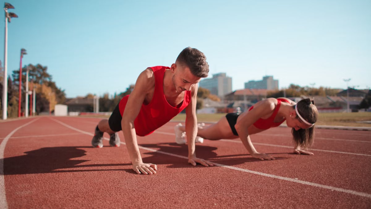 Two athletes doing push-ups on a track during daytime workout session outdoors.