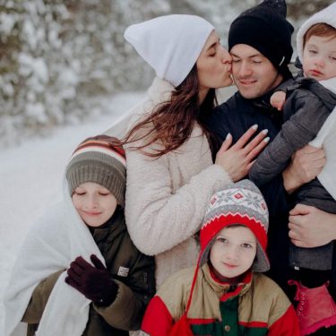 A joyful family enjoying a snowy day in a forest, wrapped in warm clothing.