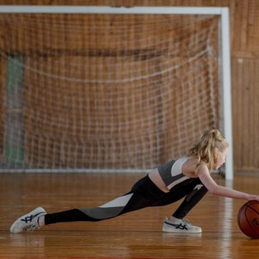 A young girl stretching with a basketball in an indoor sports hall.
