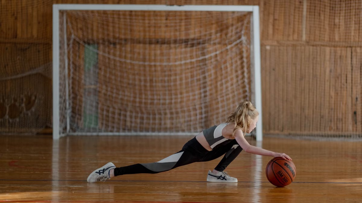 A young girl stretching with a basketball in an indoor sports hall.