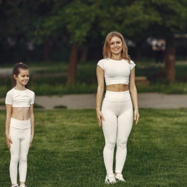 A woman and girl in white activewear standing on a grass field outdoors, smiling.